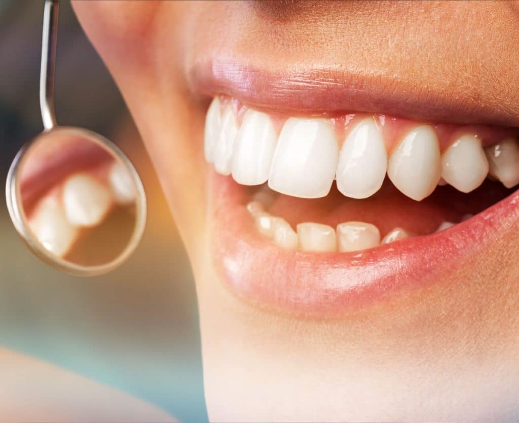 Smiling person showcasing healthy teeth with dental mirror reflecting gum health, relevant to periodontics and gum disease treatment at Hastings Dental Center.
