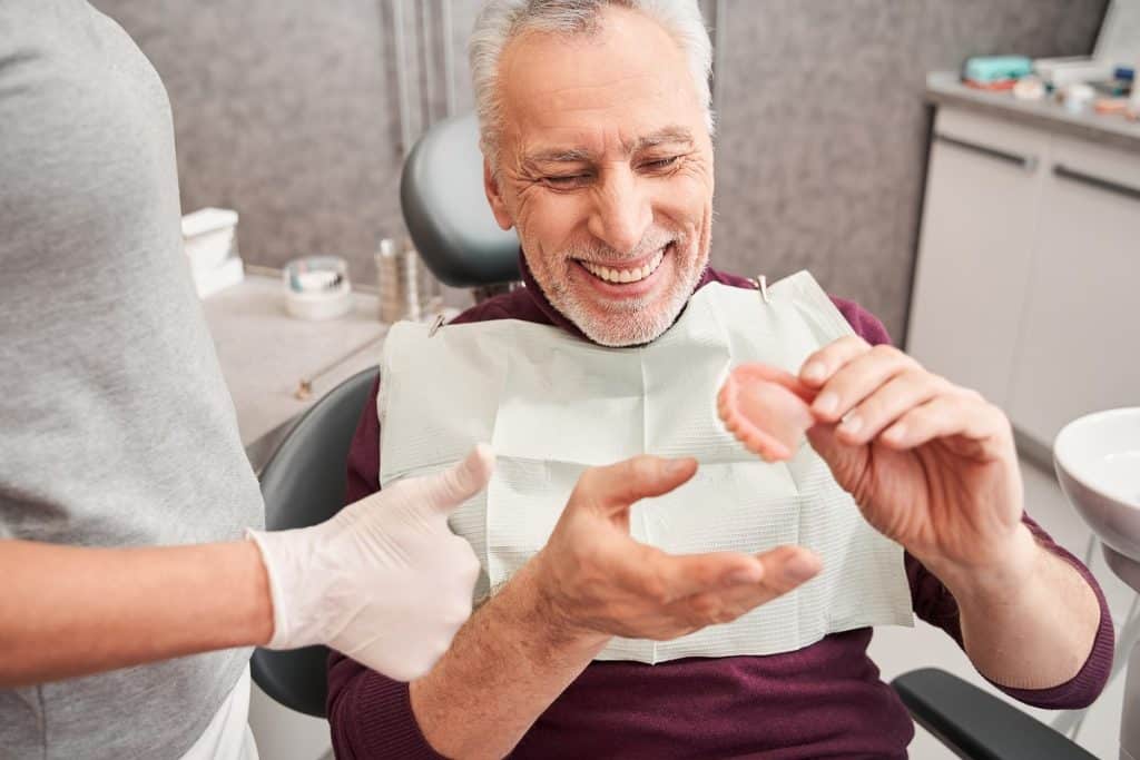 Man smiling with dentures in dental chair, demonstrating denture care and oral health.