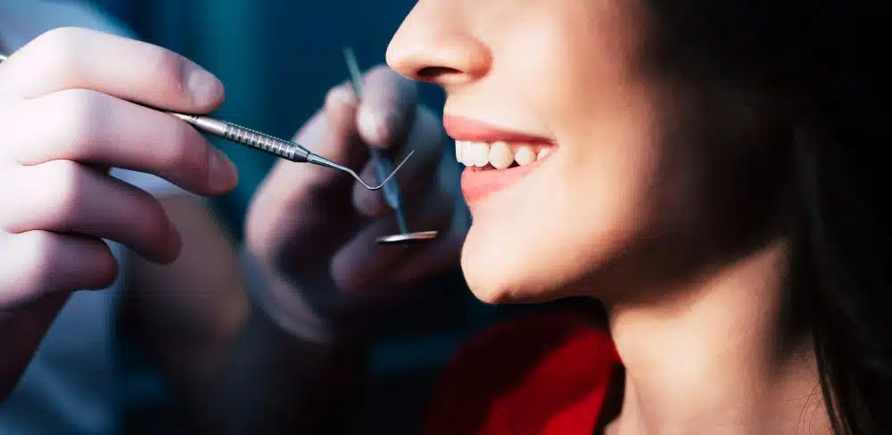 Dentist examining a woman's dental veneers with tools, showcasing a bright smile and dental care focus.