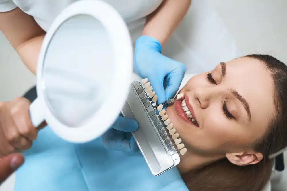 Patient receiving dental shade matching for cosmetic treatment, comparing tooth colors with a shade guide in a dental office setting.